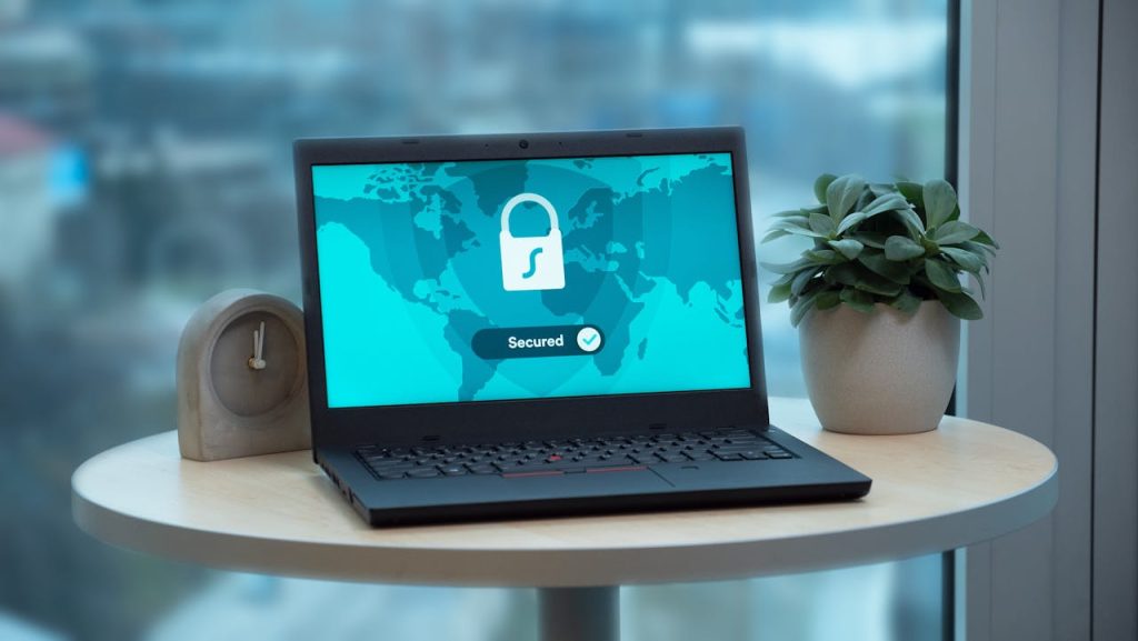 pexels photo 4973899 Laptop displaying a security lock icon on a table with a potted plant and clock.